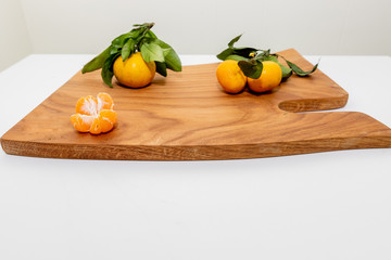 Fresh juicy clementine mandarins, winter time fruits.Half-peeled mandarin and peel on a wooden surface, minimalistic still life. Mandarine or tangerine with leaves on wooden board