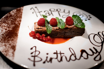a amazing chocolate brownie decorated with raspberry's and mint leaves and happy birthday written in chocolate