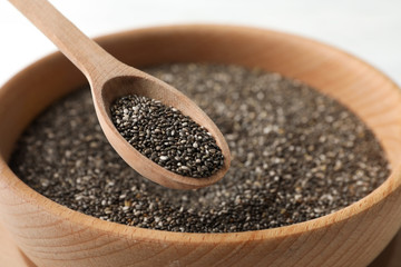 Wooden bowl with chia and spoon on white wooden background, close up