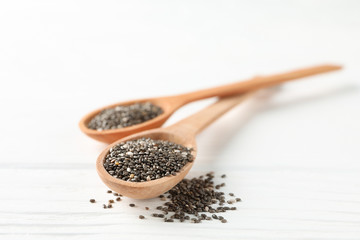 Chia seeds and wooden spoons on white wooden background, copy space