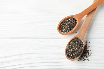 Chia seeds and wooden spoons on white wooden background, copy space