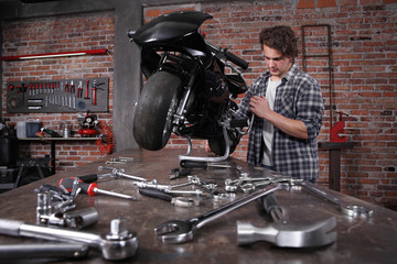 do it yourself, young man repairing a motorcycle in the garage with red brick wall, pegboard work tools and wrenches on the work bench, concept of ability and success