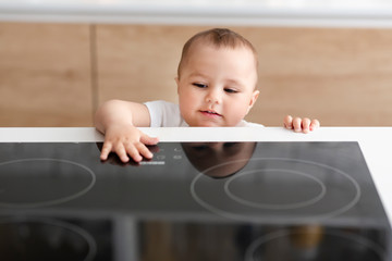 Curious toddler reaching hand to hot electric cooktop