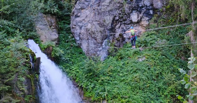 Woman moving slowly and steady, finding balance on a suspended via ferrata wire bridge towards the fierce Talbach waterfall in Austria.