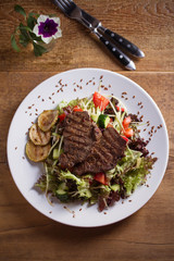 Beef salad: grilled beef steaks with tomatoes, cucumbers, zucchini, lettuce and cabbage, sprinkled with flax seeds. Overhead, vertical image