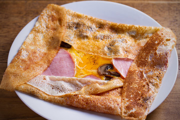 Crepes, thin pancakes with ham, cheese, egg,  and mushrooms. Pancakes with filling on white plate