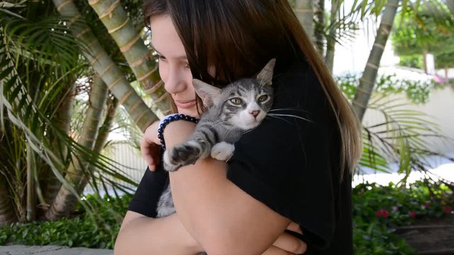 Cat laying in the arms of teengirl. Teengirl in black shirt standing by a street holding a cat snuggled in her arms like a baby.
