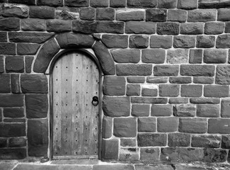 monochrome image of an ancient wooden door in a stone medieval wall