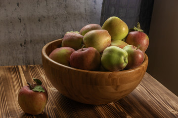 Green and red apples in a wooden bowl on wooden table. Autumn harvest set