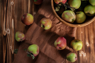 Top view of green and red apples on wooden table and brown linen cloth and wooden bowl full of fresh organic fruits. Autumn harvest set