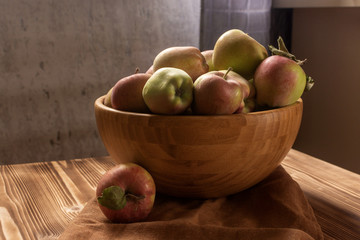 Green and red apples in a wooden bowl on wooden table. Autumn harvest set