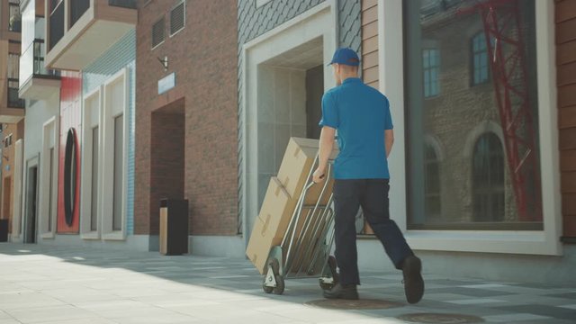 Delivery Man Pushes Hand Truck Trolley Full of Cardboard Boxes, Packages For Delivery
