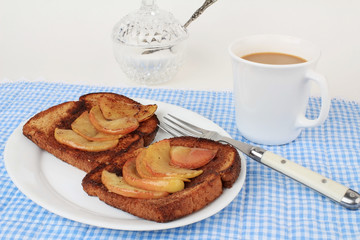 Baked apple slices on cinnamon toast with coffee and ornate sugar bowl and spoon in background.