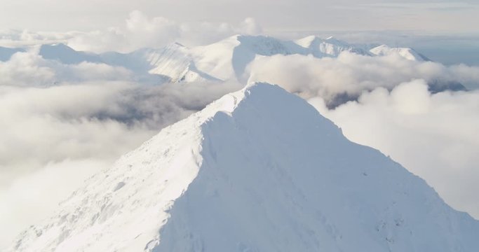 Aerial helicopter shot, track up and over snowy mountain peak to reveal bay, foggy mountains in the distance, drone footage