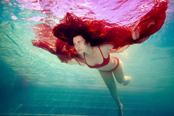Surreal portrait of a girl who swims under the water like a bird, arms outstretched, in a red...