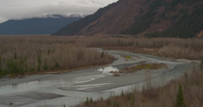 Aerial helicopter shot, slow push in on small river and gray riverbed amongst barren trees, drone footage