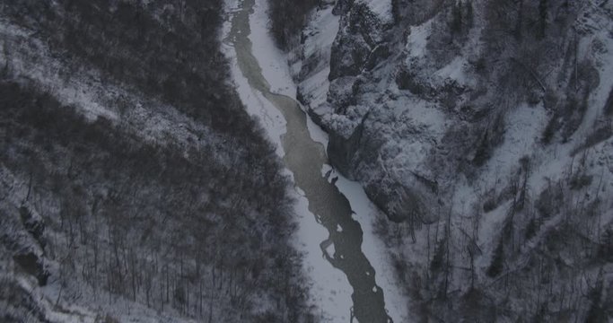 Aerial helicopter shot, fly up from frozen river in rocky Alaskan canyon to see distant mountains, drone footage