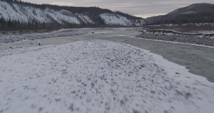 Aerial helicopter closup shot of partially frozen river with icebergs running through valley, drone footage