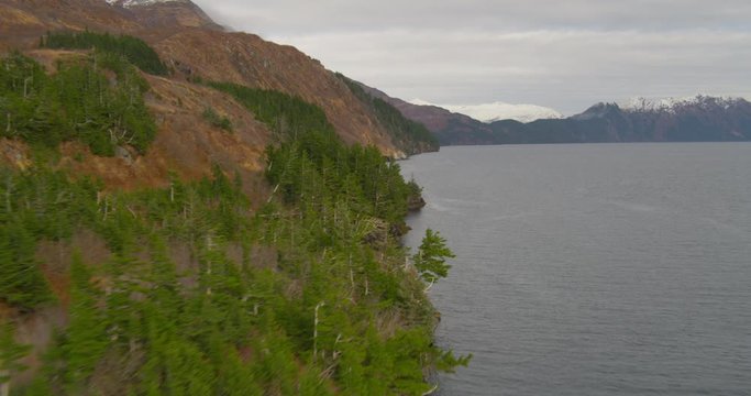 Aerial helicopter shot, past orange hillside and large Alaskan lake, evergreens, drone footage