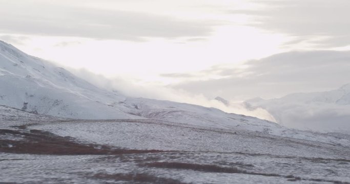 Aerial helicopter shot over snowy plateau, past steamy clouds rolling off mountainside, drone footage