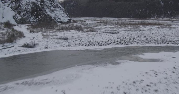 Aerial helicopter closup shot of partially frozen river with icebergs running through valley, drone footage