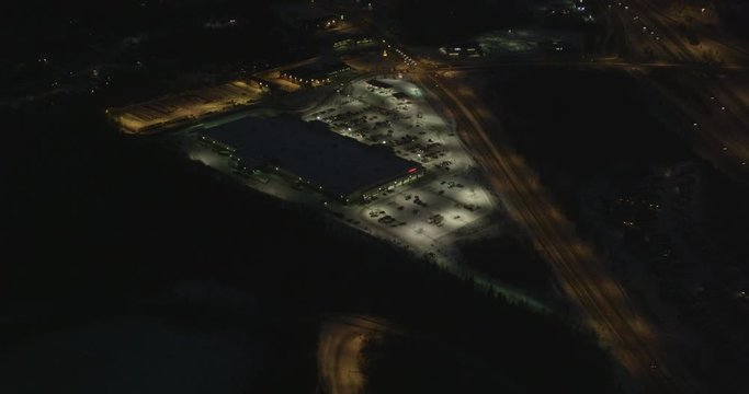 Aerial helicopter shot, push in on illuminated shopping center at night, drone footage