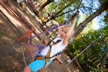 Naklejka na ściany i meble Little boy overcomes the obstacle in the rope park.