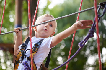 Little boy overcomes the obstacle in the rope park.