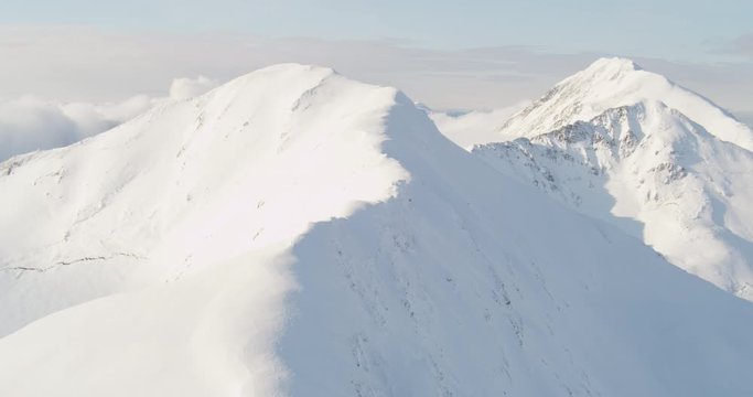 Aerial helicopter shot, push in on snowy mountain peak, reveals craggy mountain peak, drone footage