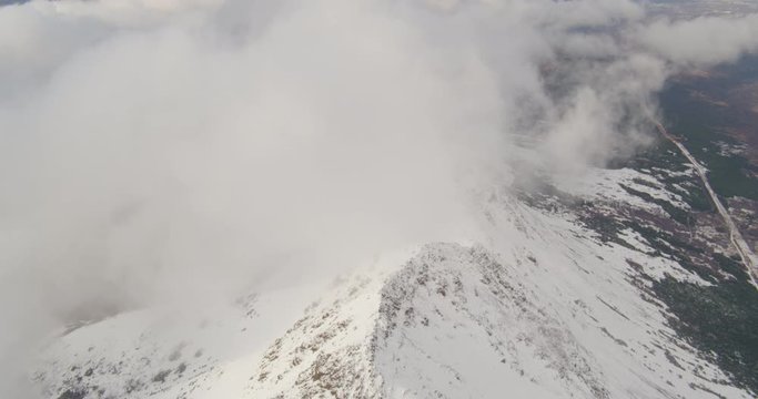 Aerial helicopter shot, tilt up from Alaskan mountain peak, zoom in on the city of Anchorage through the clouds, drone footage
