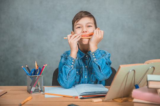 Little cheerful kid playing around with pencils during learning process. Stack of books and pecils on the desk.