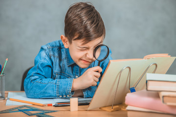 Inquisitive little boy is looking through magnifying glass at something in his book like detective.