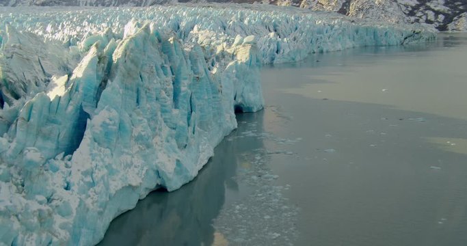  Aerial helicopter closeup details of glacial ice spires in mountain lake at golden hour, drone footage