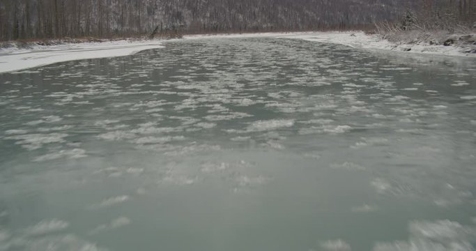  Aerial helicopter shot flying low over icy river, ice floes on water, trees, snow and tundra on banks, bridge in distance around the bend, drone footage