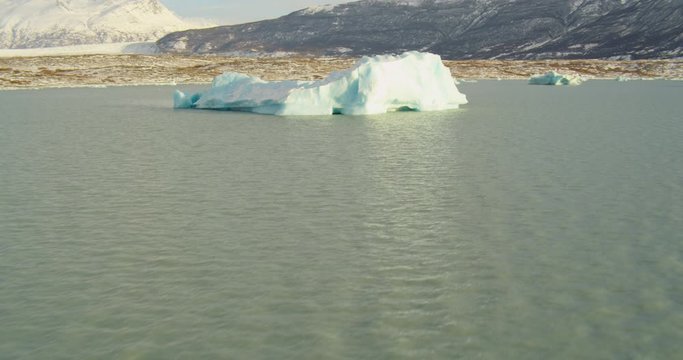  Aerial helicopter shot, fly close adjacent to iceberg in mountain lake at golden hour and towards others in lake, drone footage