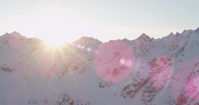  Aerial helicopter shot, tracking across a rocky, snowy Alaskan mountain range cast in shadow during golden hour, drone footage, lens flare
