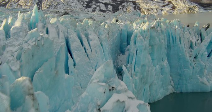  Aerial helicopter closeup details of glacial ice spires in mountain lake at golden hour, push past the ice and down to water level, drone footage