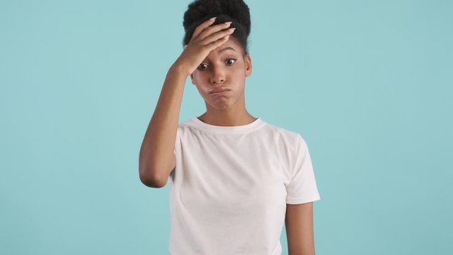 Portrait of upset african american girl  perplexedly looking in camera over blue background. Face palm expression