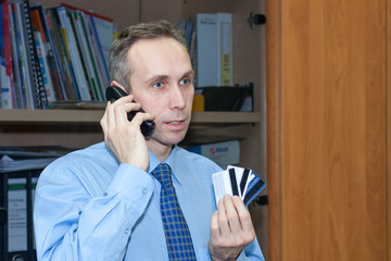 cheerful Manager holds several credit cards and talks on the phone