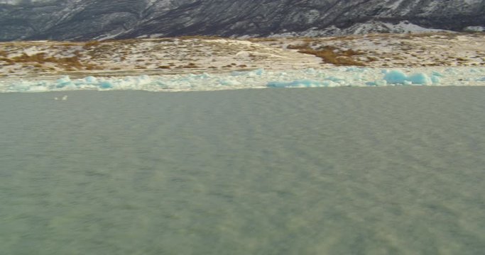  Aerial helicopter shot, over splintered ice floes and icebergs in mountain lake at golden hour and towards mountainside, drone footage