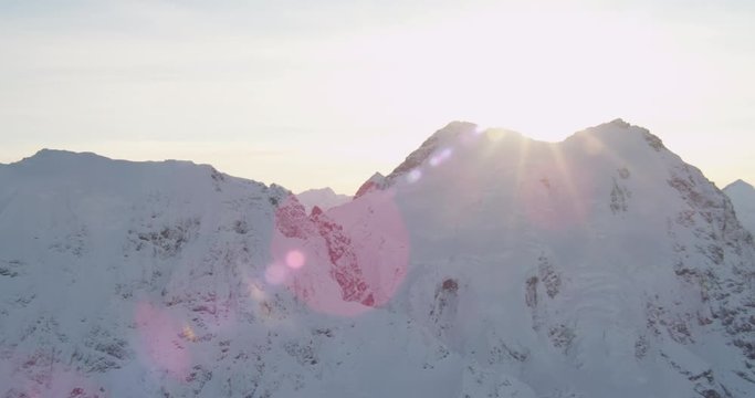  Aerial helicopter closeup shot, panning back and forth over a rocky, snowy mountain at golden hour, lens flare, drone footage