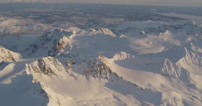  Aerial helicopter shot, panning across a vast, rocky, snowy Alaskan mountain range at golden hour, drone footage, lens flare
