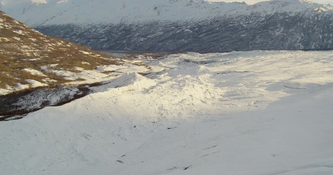  Aerial helicopter shot, pushing around corner of mountainside across rippling glacier at golden hour, drone footage