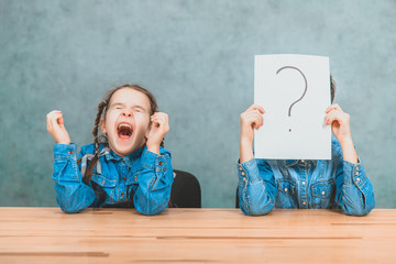 Schoolchildren sitting at the desk. Boy is hiding behind the sheet of paper with exclamation mark. Girl with funny pigtails is yawning.