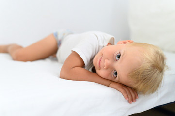 cute little smiling boy is lying on white bed