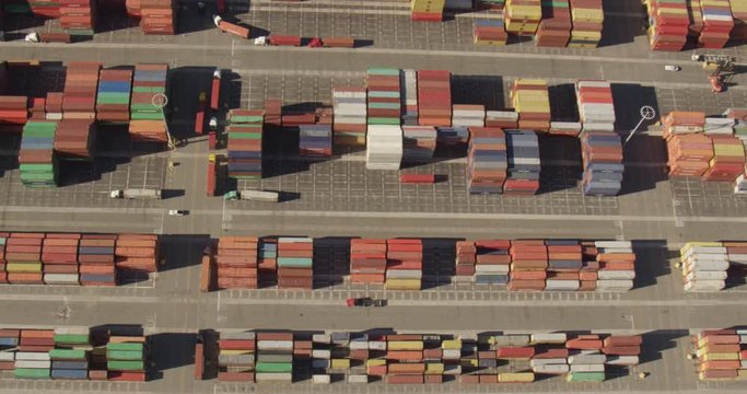 Aerial helicopter shot, overhead shot of rows of multicolored shipping containers, container tugs, semi trucks, drone footage