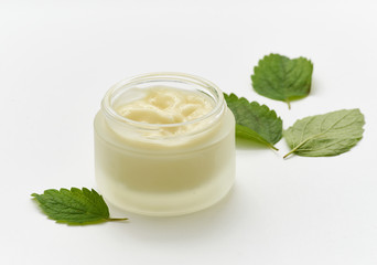 Obraz na płótnie Canvas Composition of white cream in a small jar and a few mint leaves on a white background.