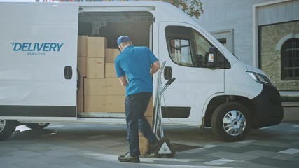 Delivery Man Uses Hand Truck Trolley Full of Cardboard Boxes and Packages, Loads Parcels into Truck / Van. Professional Courier / Loader helping you Move, Delivering Your Purchased Items Efficiently
