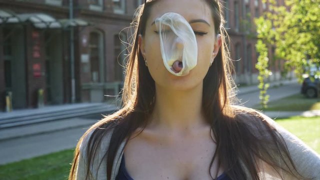 Young woman inflating a bubble of chewing gum then bubble funny bursts on the face on sunset