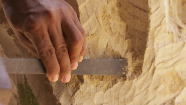 A craftsman's hands using a hammer and chisel to make a sand sculpture